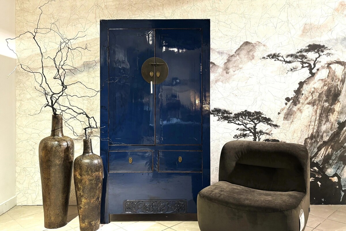 Granatowa szafa do salonu lub sypialni.  Ciekawa szafa w kolorze niebieskim. Tapeta w stylu japońskim. Brązowy fotel obrotowy. Fotel w kolorze mocha mousse. Duże wazony z gałęziami.