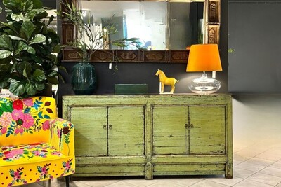 Zielona komoda. Długa komoda do slaonu w kolorze pistacjowym. Ciekawa komoda zielona. Żółty fotel w kwiaty. Lustro drewniane. Lampa z żółtym abażurem