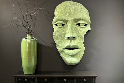 Dekoracyjna maska ścienna w zielonym kolorze. Oryginalna rzeźba twarz.  Czarna ściana w salonie. Zielona maska, płaskorzeźba na ścianę. Zielony wazon, gałęzie w wazonie.